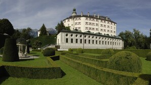 A large, classical building with a symmetrical facade, surrounded by well-manicured gardens and a mountainous backdrop. - DION Hotel Wattens (Wattens)