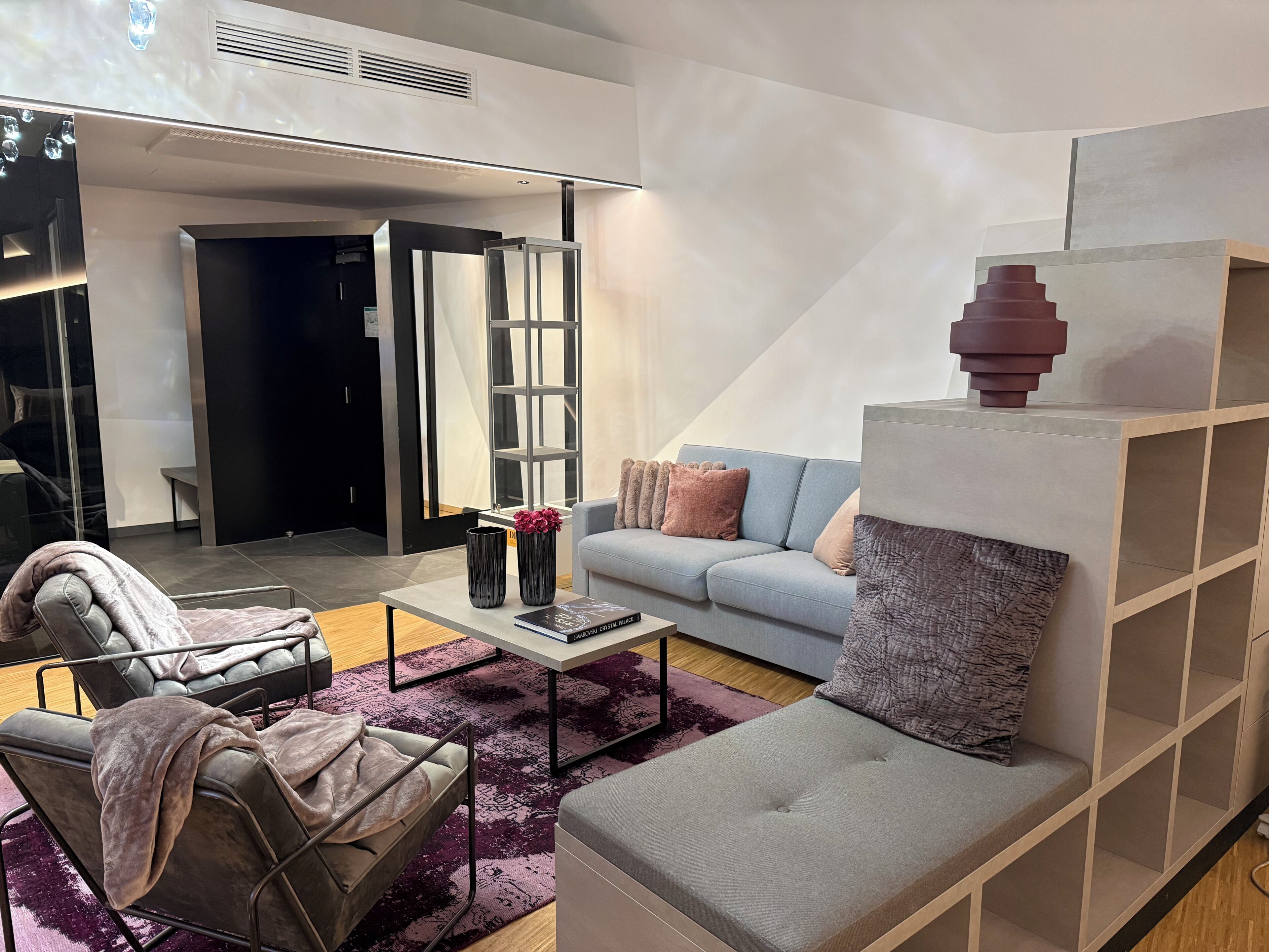Una sala de estar moderna con un sofá gris, un sillón negro, una mesa de centro con libros y un jarrón decorativo.
