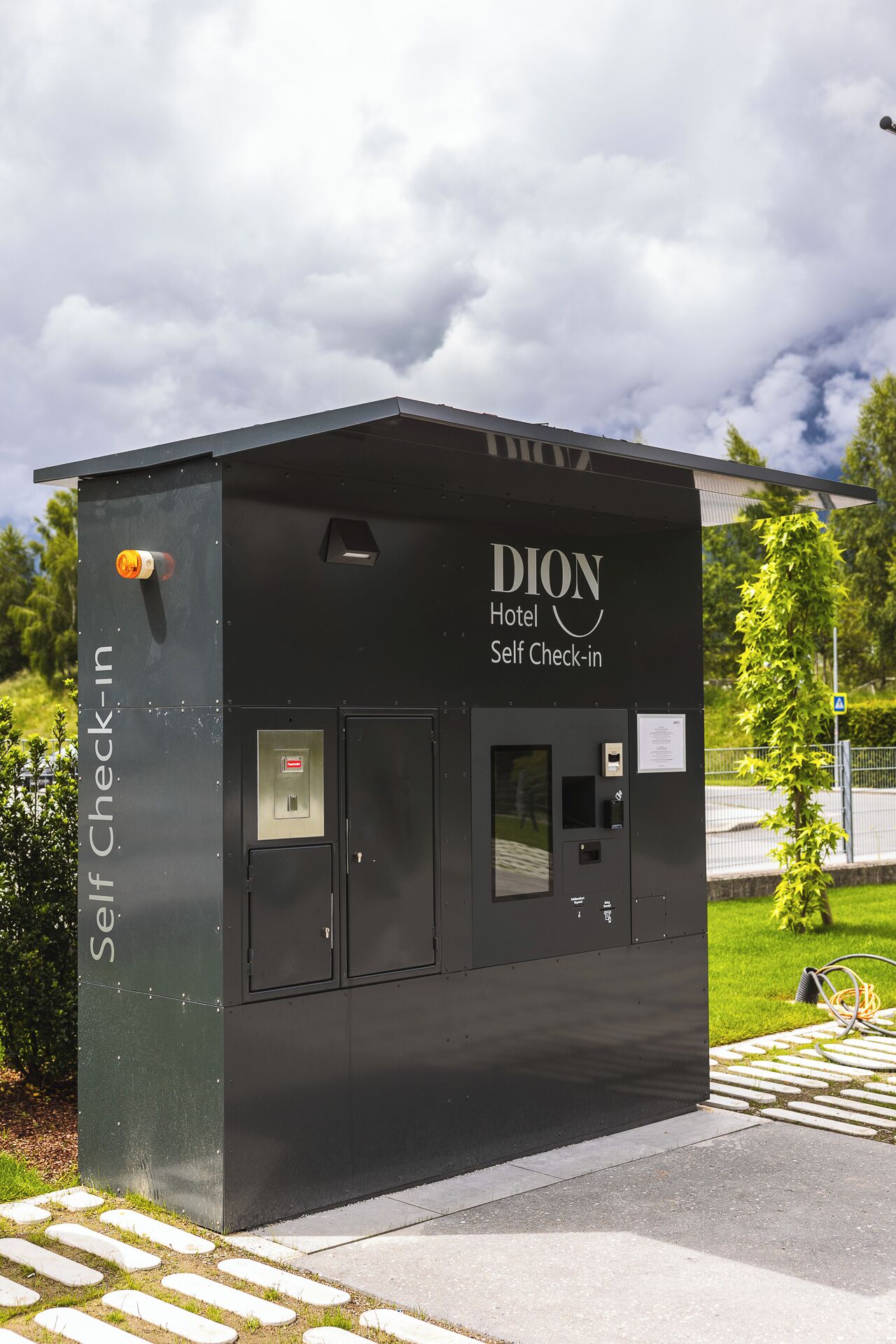 Ein Selbstcheck-in-Terminal für das DION Hotel mit Tastenfeld, kleinem Bildschirm und Tür.