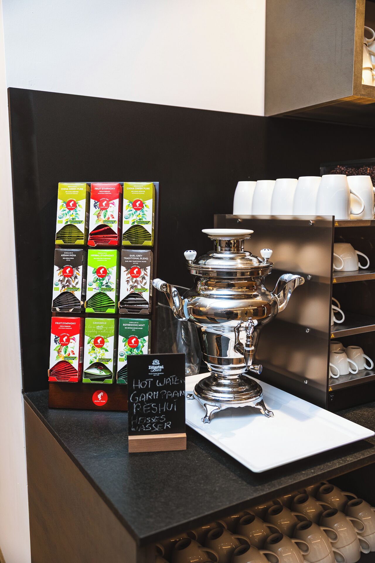 Una estación de café con una máquina de café, tazas y una variedad de cajas de té.