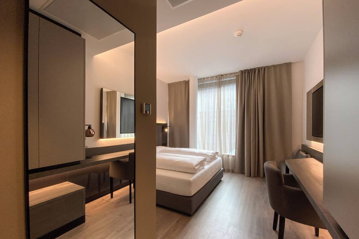 A hotel room with a bed, a desk, a chair, a mirror, and a television.