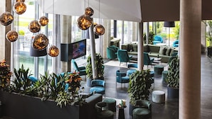 A spacious lobby with modern furniture, hanging spherical light fixtures, and potted plants. - DION Hotel Wattens (Wattens)