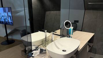 A modern bathroom with a large mirror, two sinks, a vanity, and a television.