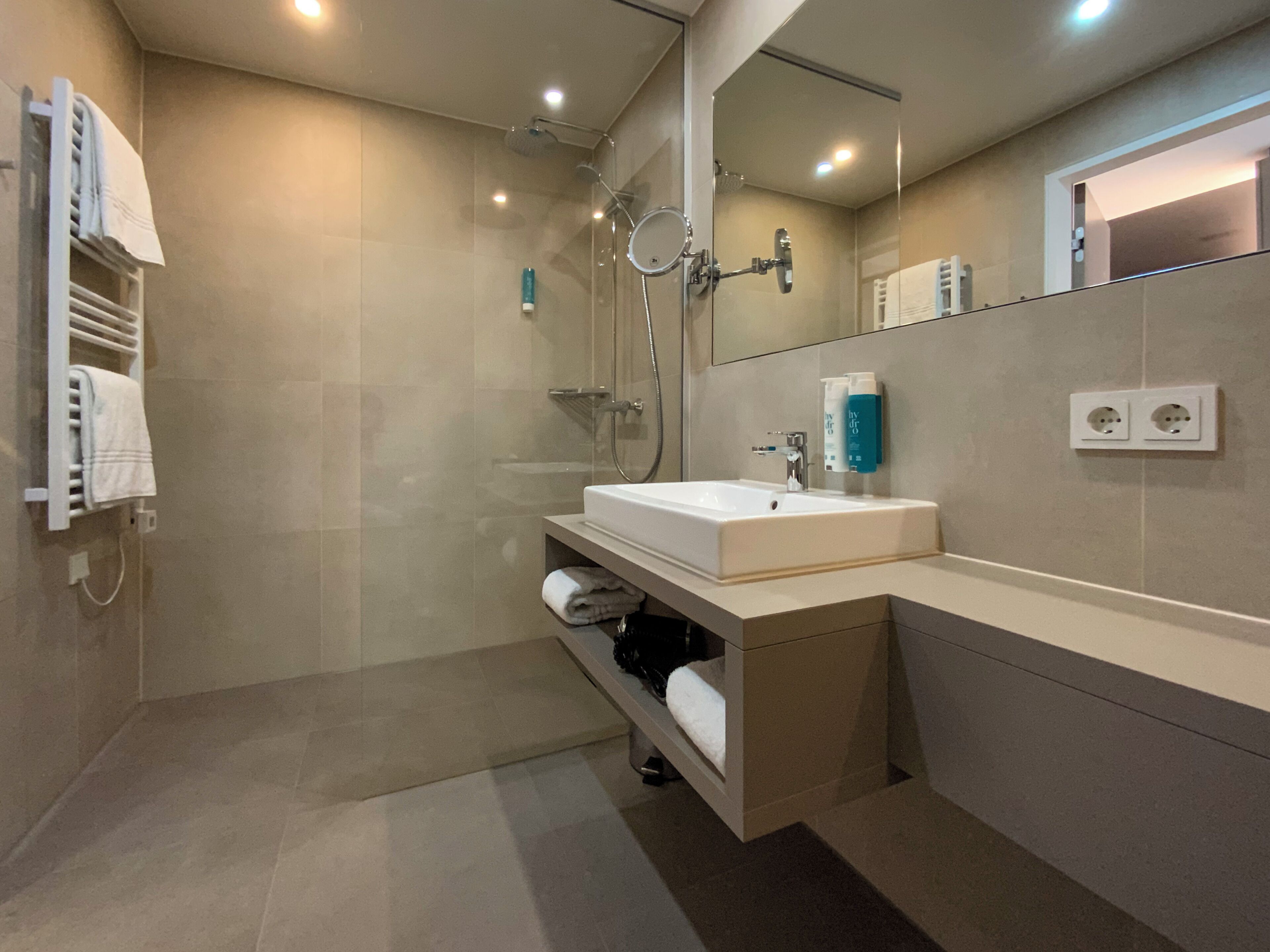 Un baño moderno con ducha de vidrio, un lavamanos blanco y un espejo encima.