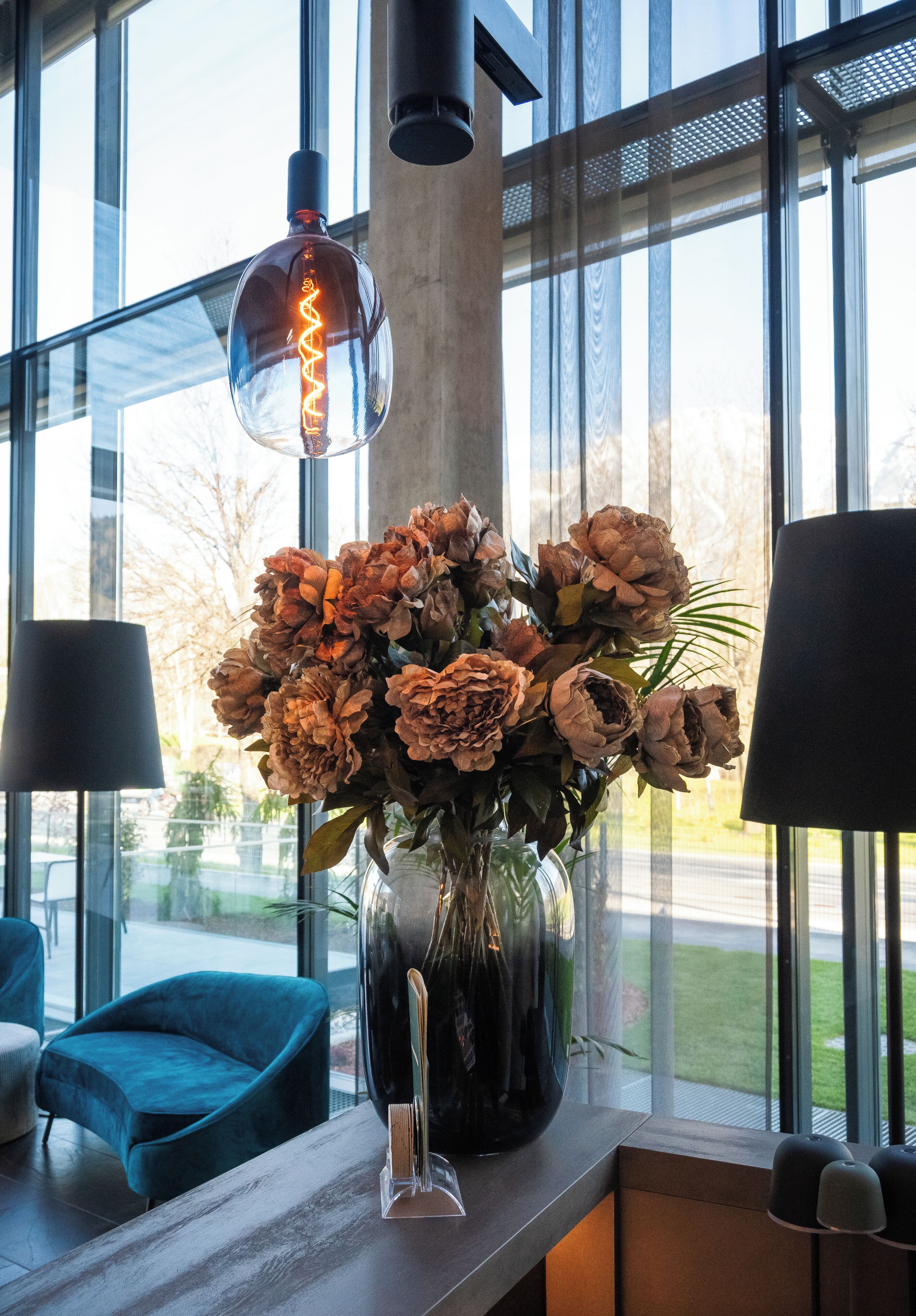 A modern interior with a large window, a vase of dried flowers, and a hanging light fixture.