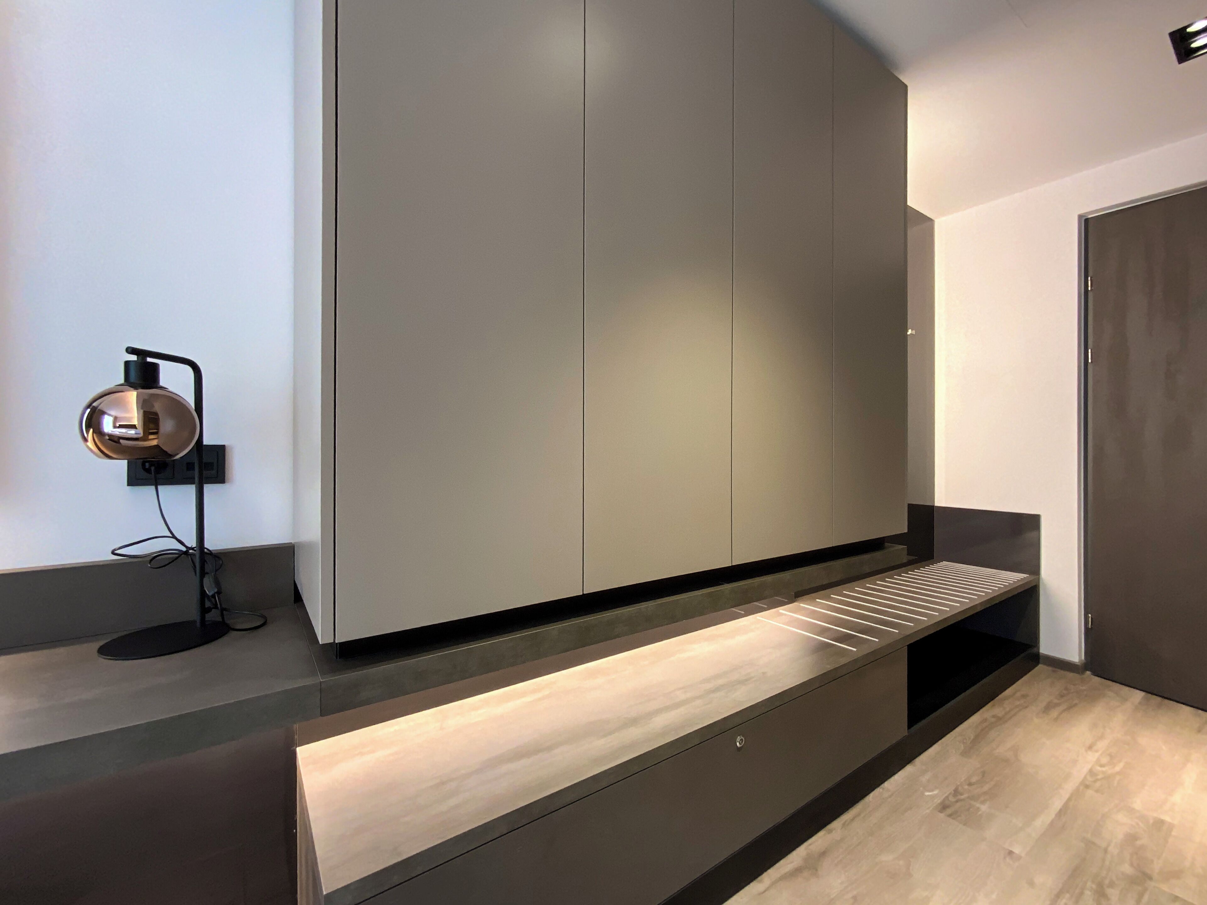 Une chambre moderne et minimaliste, dotée d’une banquette intégrée, d’une lampe fixée au mur et d’une grande armoire.