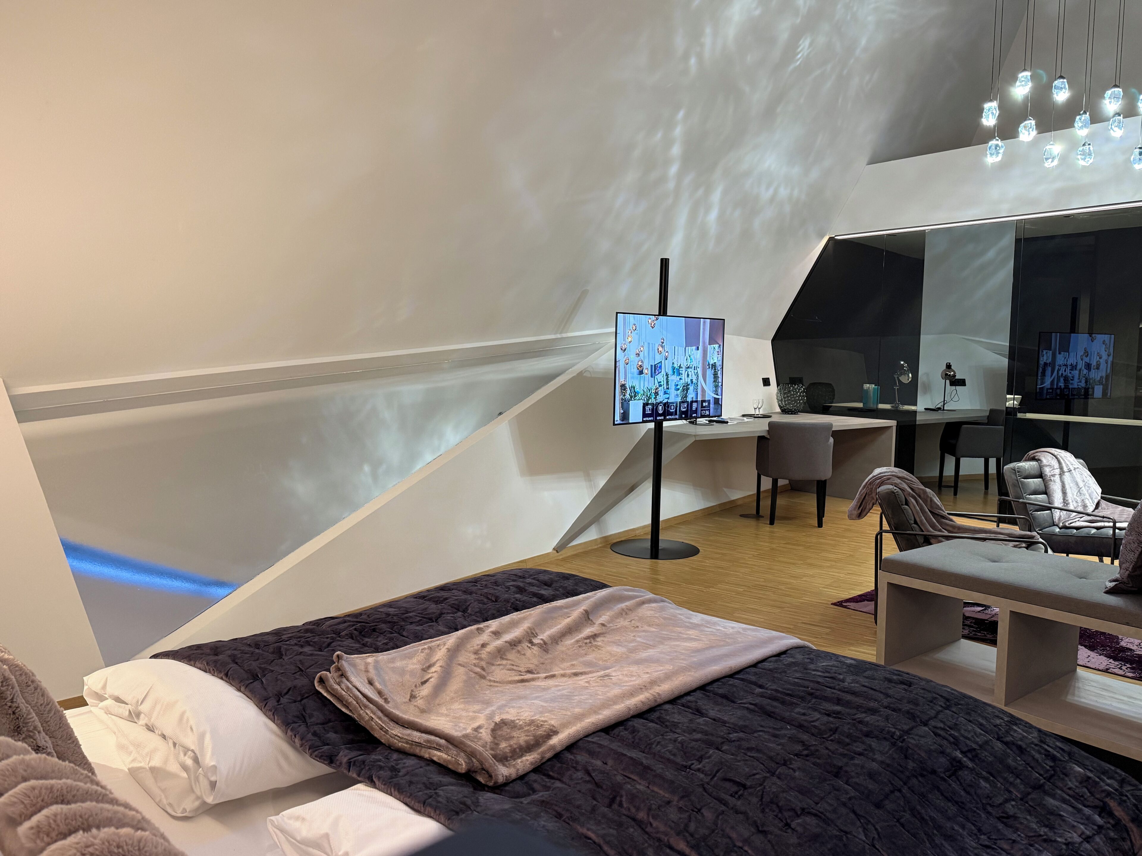A modern room with a bed, a desk, a chair, and a TV.
