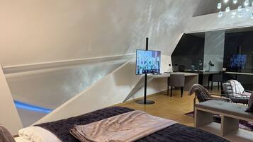 A modern room with a bed, a desk, a chair, and a TV.