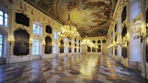 A grand hall with ornate chandeliers, large windows, and a checkered floor. - DION Hotel Wattens (Wattens)
