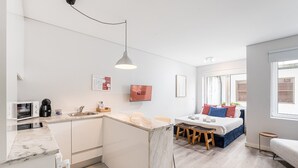 Eine kompakte, moderne Wohnung mit Küchenzeile, einem Bett mit blauem Kopfteil und einer kleinen Essecke.