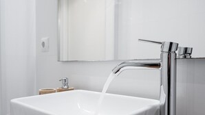 Ein modernes Badezimmer mit einem weißen Waschbecken, einem Chromarmaturen-Set und einem Spiegel darüber.