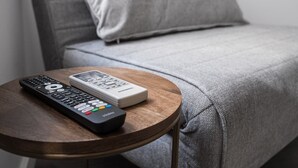 Ein graues Sofa mit Fernbedienung und einem weißen Gerät auf einem runden Holztisch.