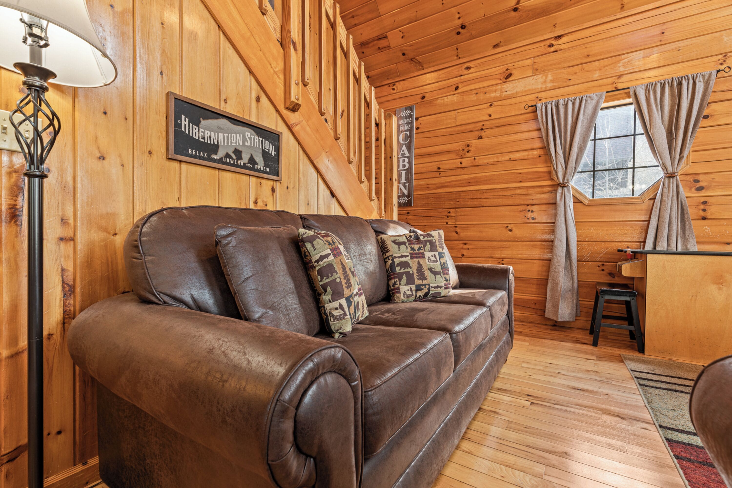 A wooden cabin interior with a leather sofa, a lamp, and a sign reading "Hibernation Station".
