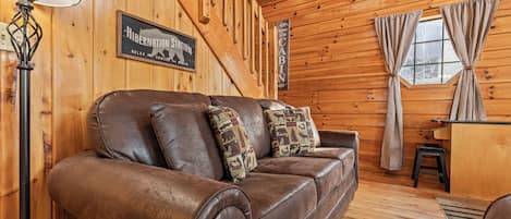 A wooden cabin interior with a leather sofa, a lamp, and a sign reading "Hibernation Station".