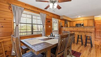 A wooden interior with a dining table, chairs, a ceiling fan, and a kitchen area with wooden cabinets and a microwave.