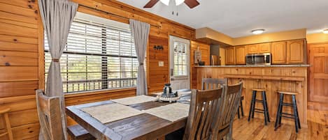 A wooden interior with a dining table, chairs, a ceiling fan, and a kitchen area with wooden cabinets and a microwave.