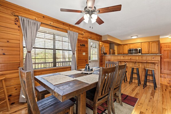 Un intérieur en bois comprenant une table à manger, des chaises, un ventilateur de plafond et un coin cuisine avec des placards en bois et un four à micro-ondes.
