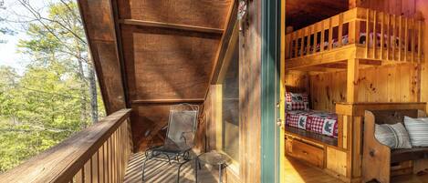 A wooden cabin with a balcony, a bed with a checkered bedspread, and a chair.