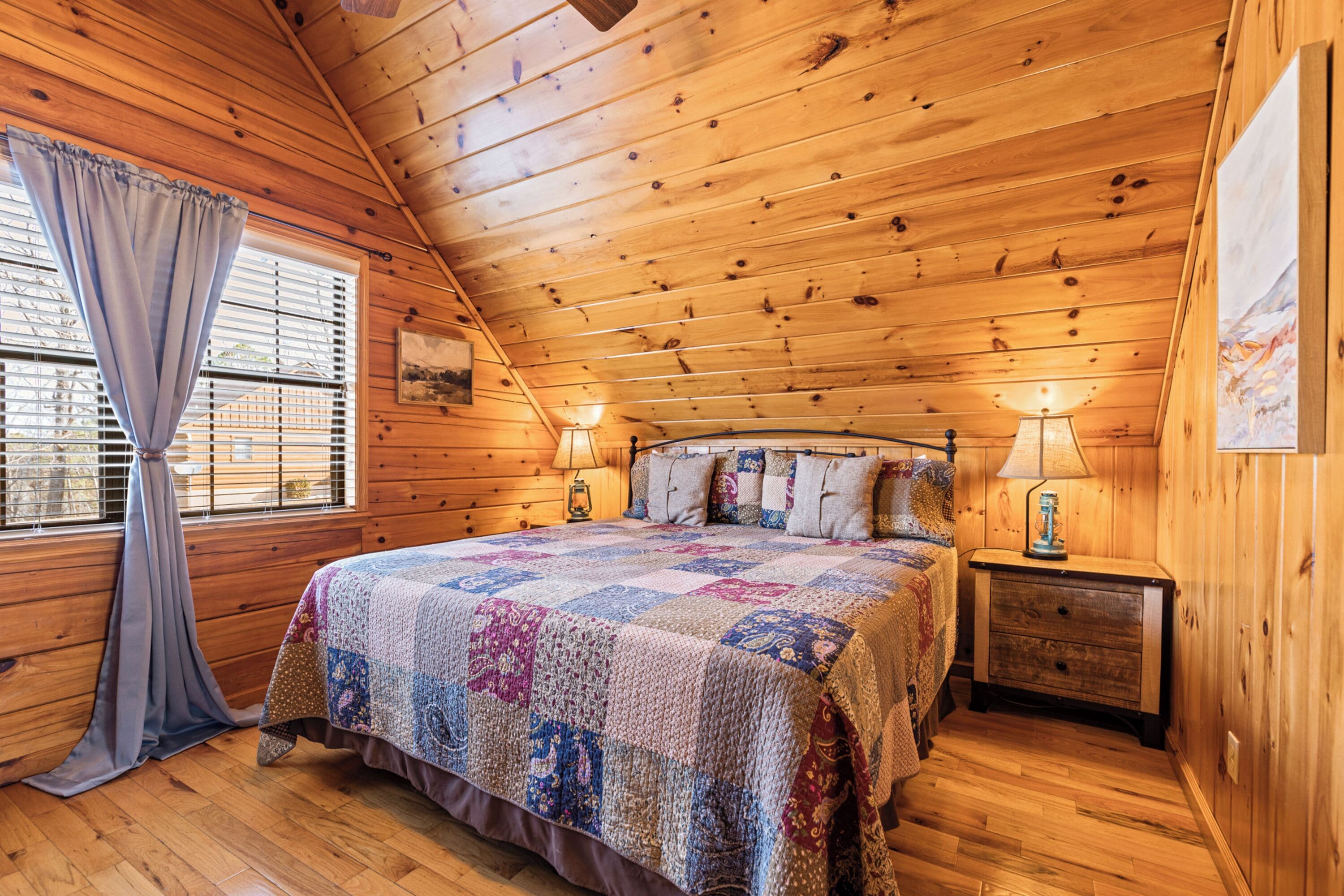 Ein gemütliches Schlafzimmer in einer Holzhütte mit einem großen Bett, zwei Nachttischen mit Lampen und einem Fenster mit Vorhängen.