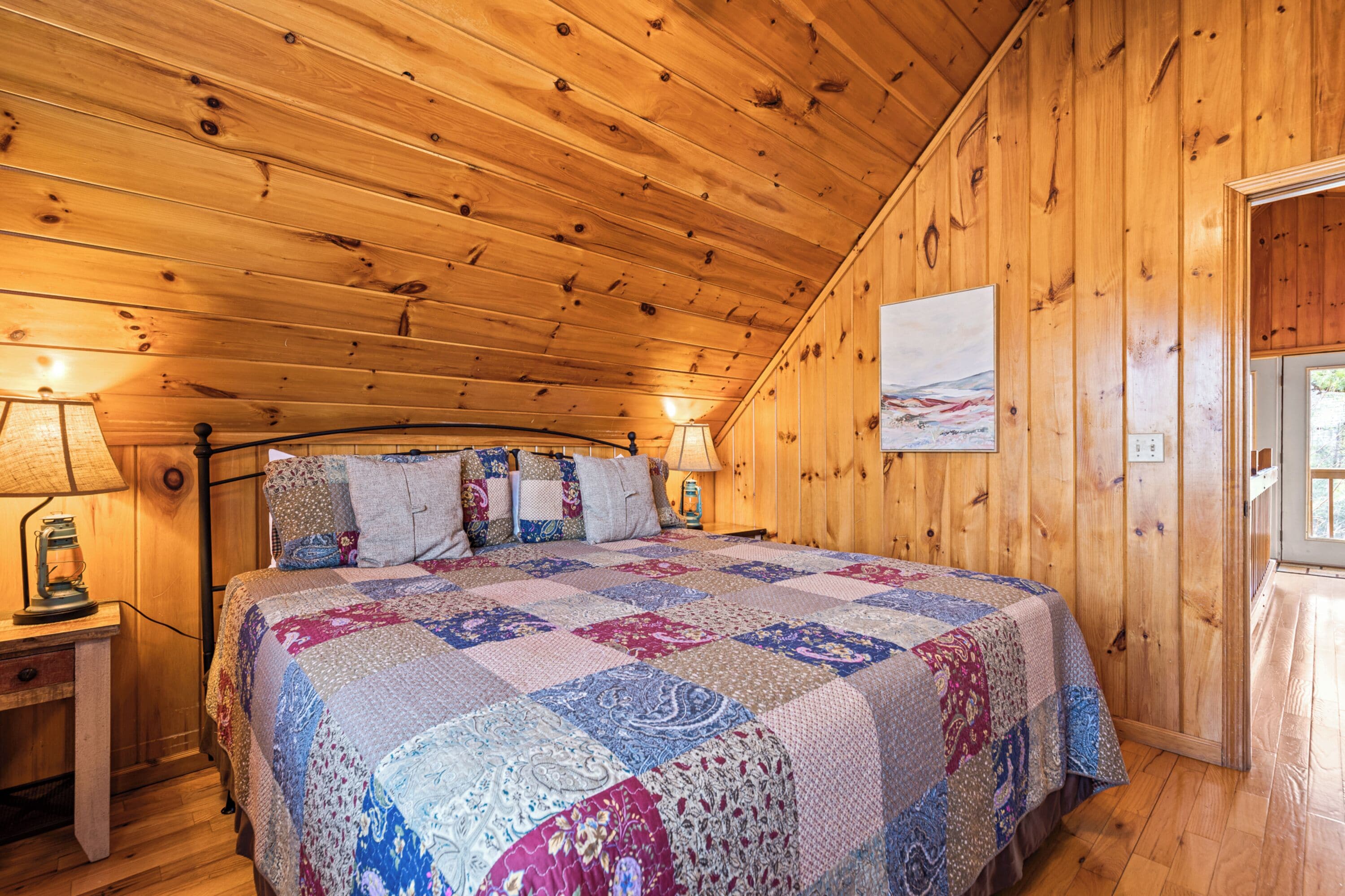 A wooden cabin bedroom with a large bed, wooden walls, and a window.