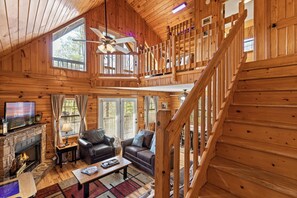L’intérieur d’un chalet en bois, avec une cheminée, un canapé, une table basse et un téléviseur.
