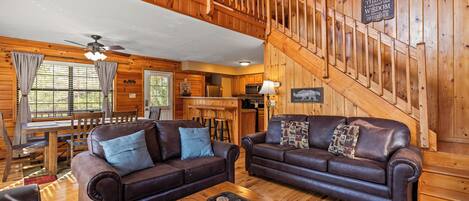 A wooden cabin interior with two leather sofas, a dining table, and a staircase.