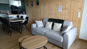 Una sala de estar con un sofá gris, dos mesas redondas de madera y una mesa de comedor de madera con sillas.