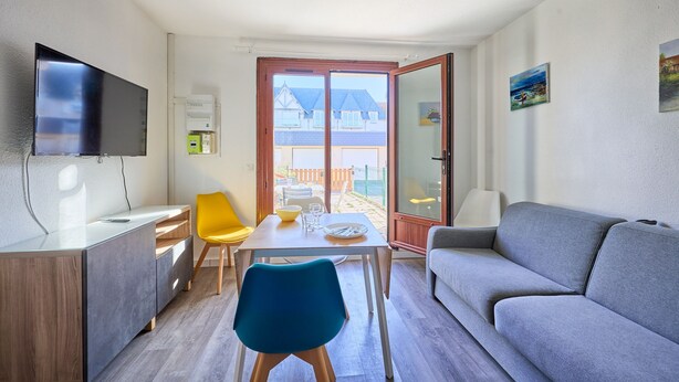 A modern living room with a grey sofa, a blue chair, a wooden cabinet, and a flat-screen TV mounted on the wall. - L'Ancre Bleue - Duplex à 10min de la plage (Courseulles-sur-Mer)