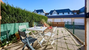 An outdoor patio with a table and chairs, a green fence, and a view of houses in the background. - L'Ancre Bleue - Duplex à 10min de la plage (Courseulles-sur-Mer)