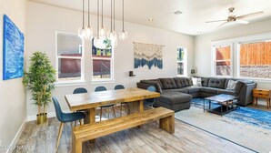 Un vaste salon comprenant une table à manger en bois, un canapé d’angle gris et un ventilateur de plafond.