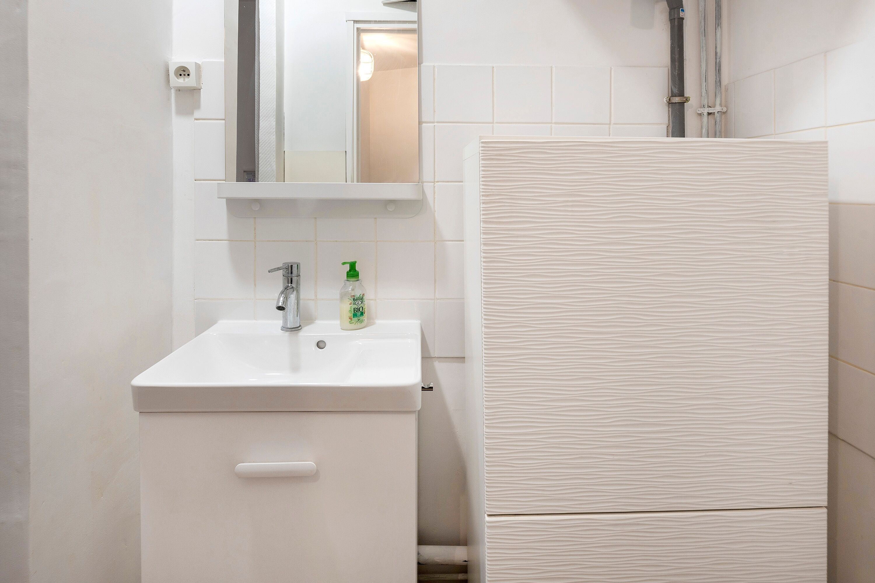 A bathroom with a white sink, mirror, and a shower area with a textured wall.
