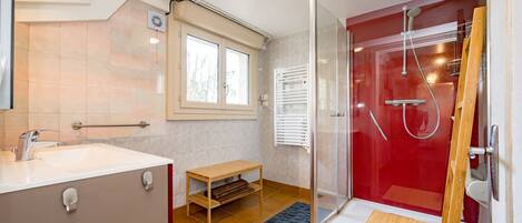 A bathroom with a shower, a sink, a window, and a small wooden table.
