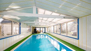 An indoor swimming pool with clear glass walls, a tiled floor, and a ceiling with skylights.