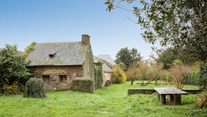 Una casa in pietra con tetto spiovente, immersa in un prato e con un piccolo tavolo di legno.