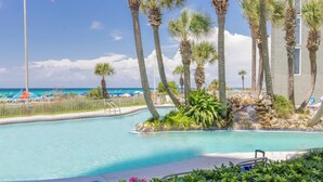A pool area with a view of the beach, palm trees, and a small waterfall.