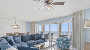 A spacious living room with a large sectional sofa, a coffee table, and a view of the ocean through large sliding glass doors.