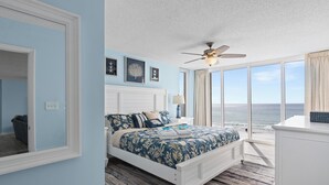 A bedroom with a large bed, a ceiling fan, and a view of the ocean.
