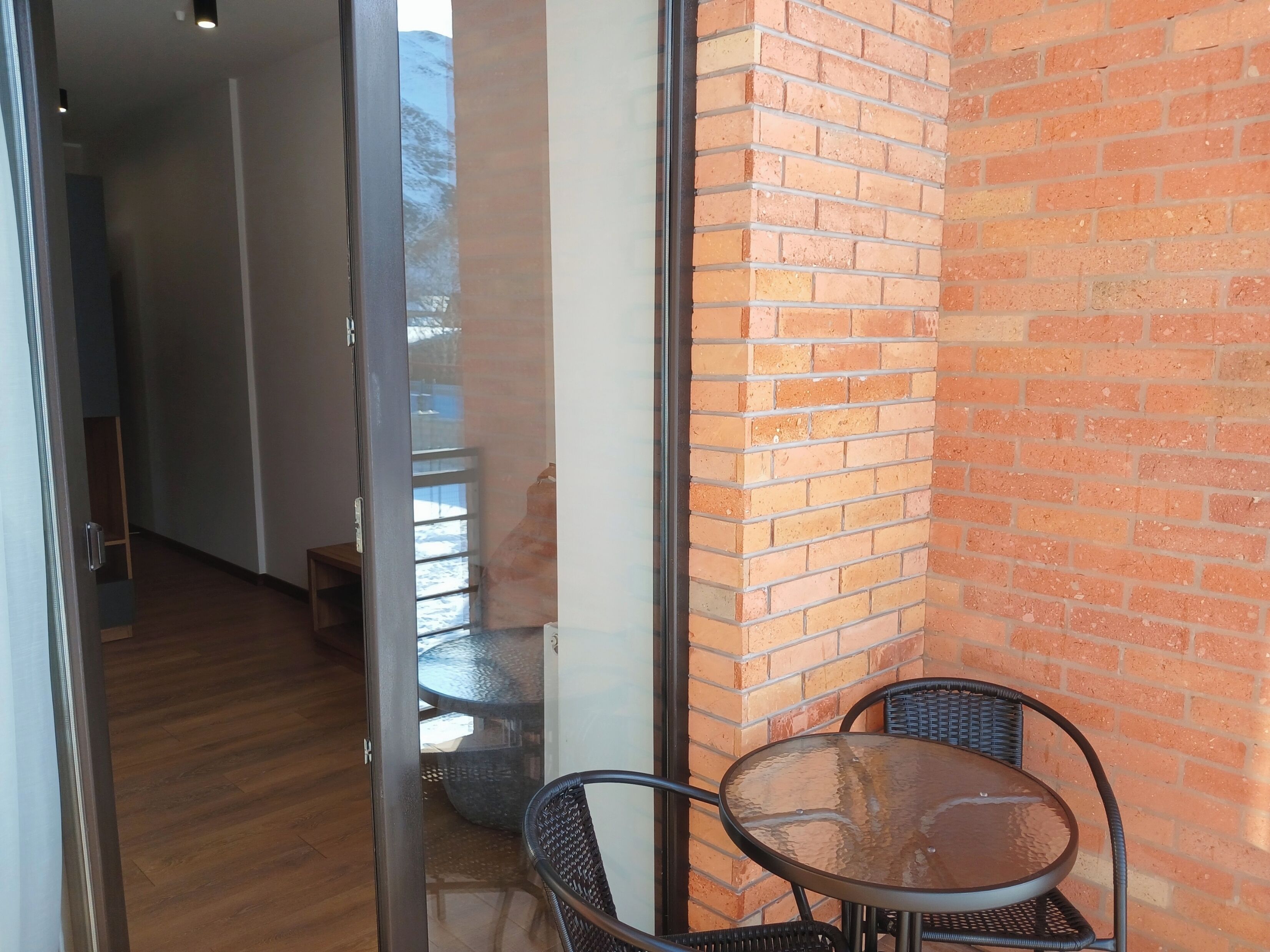 A corner of a room with a glass door leading to a balcony, a brick wall, and a round table with chairs.
