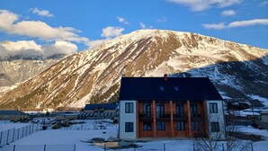 A modern building with a flat roof and multiple windows, situated in a snowy landscape with a mountain in the background. - AGRE Kazbegi (Kazbegi)
