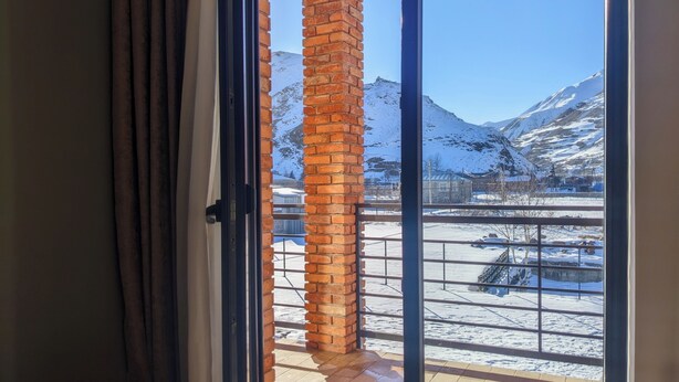 A room with a large window, a brick pillar, and a view of snow-covered mountains. - AGRE Kazbegi (Kazbegi)