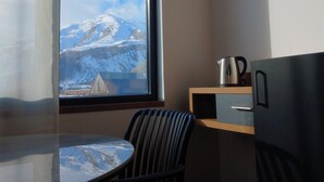 A room with a view of a snow-capped mountain, a table, a chair, a kettle, and a cabinet. - AGRE Kazbegi (Kazbegi)