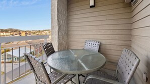 Un balcon avec une table ronde en verre et quatre chaises, donnant sur une rue et des immeubles.