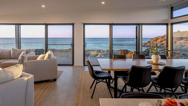 A modern living room with a large dining table, comfortable seating, and a scenic ocean view through large windows. - Cove Landing Ocean View Apt-1,2&3 Sleeps 12 (Penneshaw)