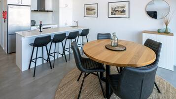 A modern kitchen with white cabinets, a central island with bar stools, a dining table with chairs, and artwork on the walls.