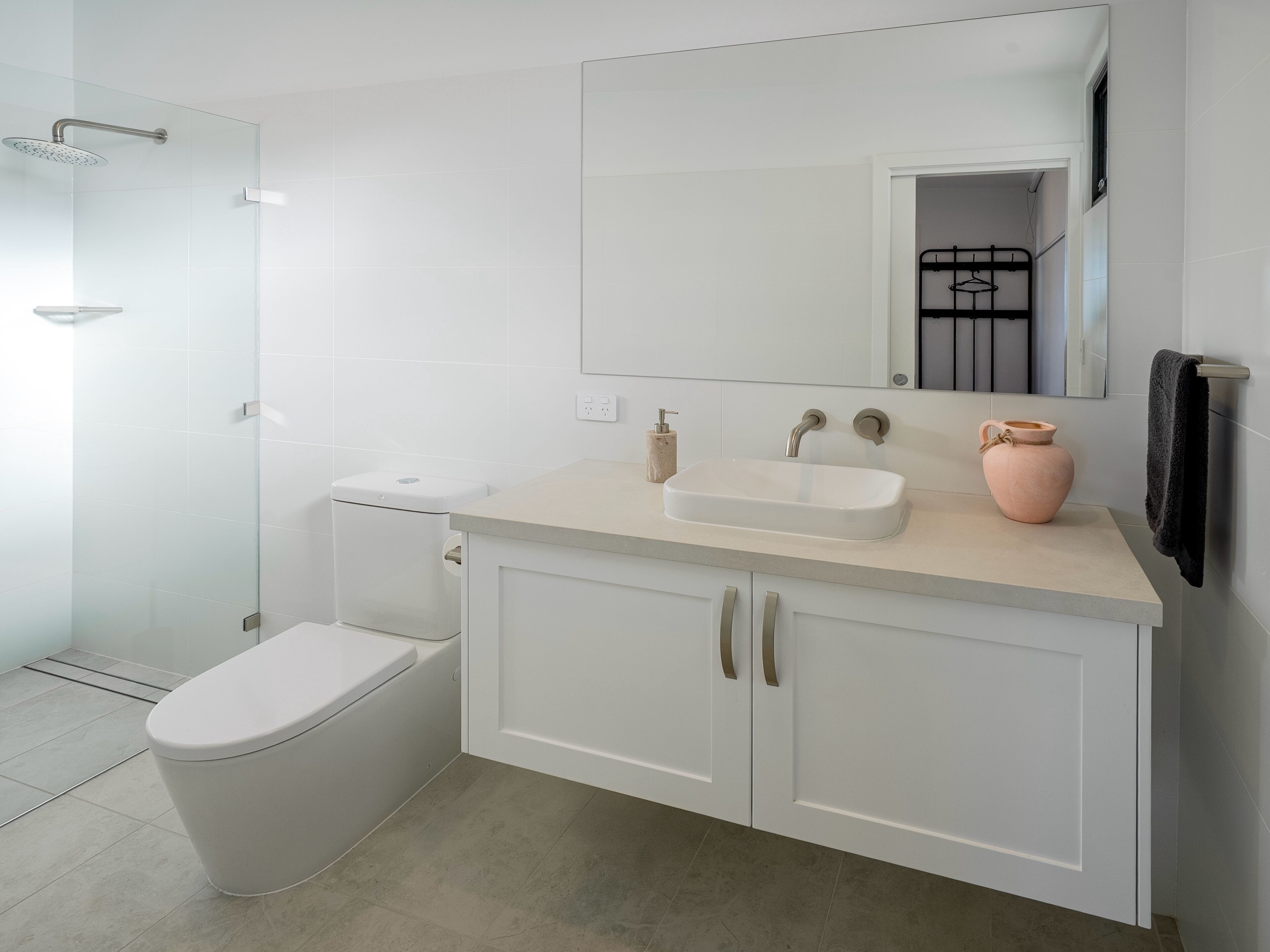 Ein modernes Badezimmer mit einer Duschkabine aus Glas, einer weißen Toilette, einem Waschbecken mit Spiegel darüber und einem Schrank mit zwei Türen.
