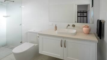 Ein modernes Badezimmer mit einer Duschkabine aus Glas, einer weißen Toilette, einem Waschbecken mit Spiegel darüber und einem Schrank mit zwei Türen.