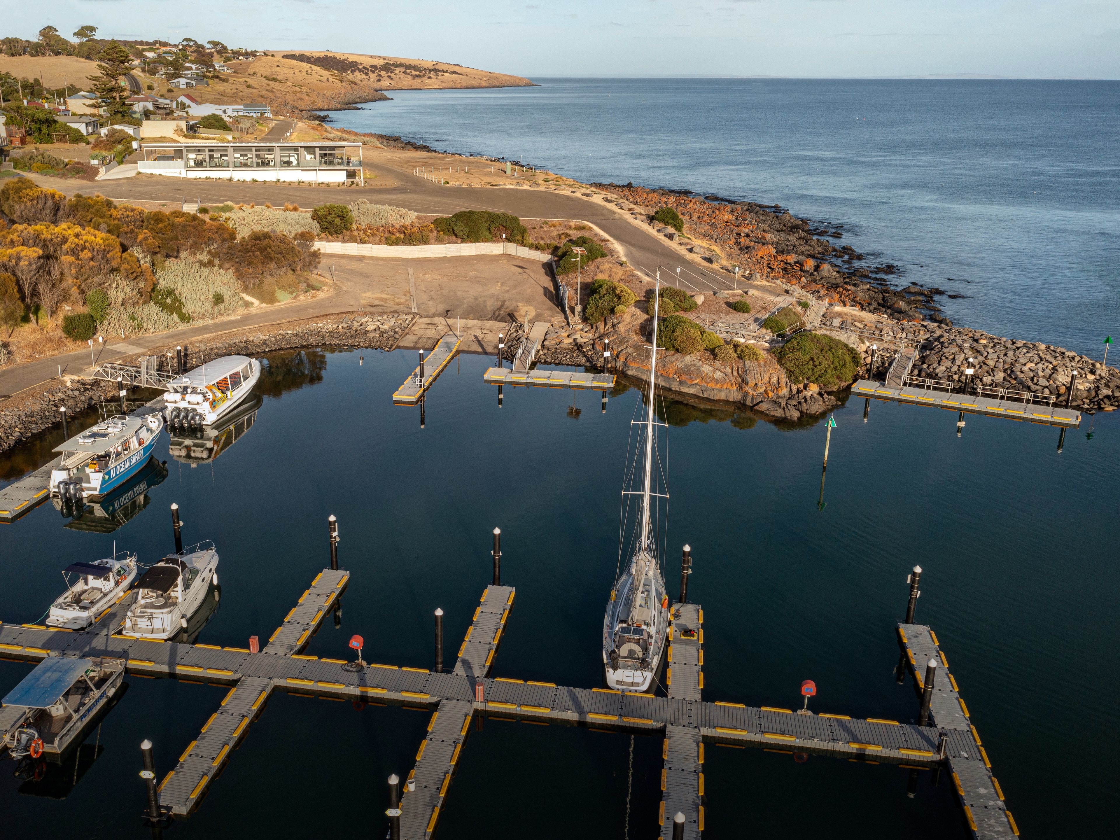 Un port de plaisance doté de plusieurs quais et abritant de nombreux bateaux, entouré d’un paysage vallonné et offrant une vue dégagée sur l’océan.