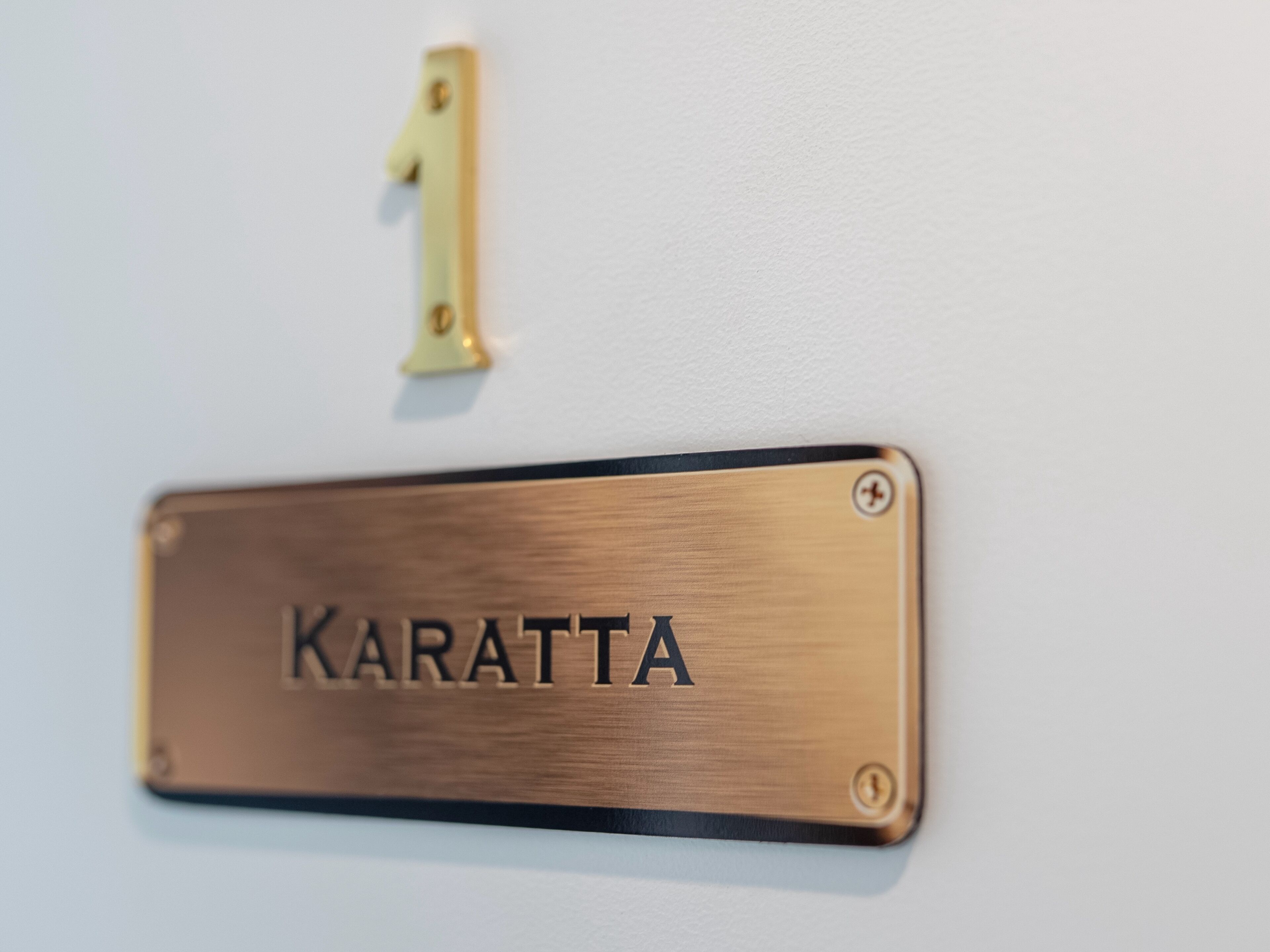 Eine Namensplakette aus Messing mit dem Wort 'Karatta' an einer Wand befestigt.