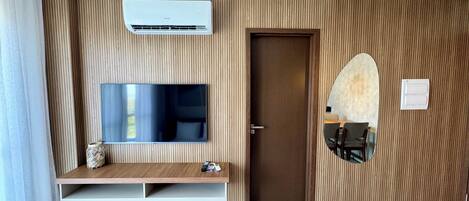 Una sala de estar moderna con un televisor montado, paneles de madera empotrados, una puerta y un estante pequeño con adornos.