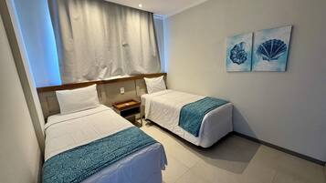 A hotel room with two single beds, a nightstand, a bedside table, and two wall-mounted artworks.